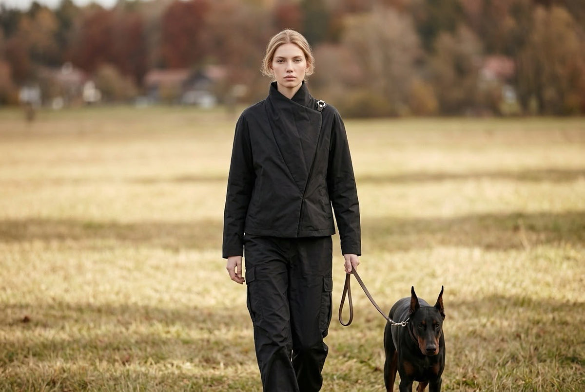 Woman walking a dog across an autumn field in a black padded jacket and black trousers, TOFUITO Fall/Winter 2026