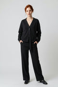 The Axis Drop Jacket – front view of the black V-neck jacket, hands in pockets, with wide-leg trousers