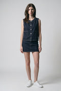 Front view of The Halo Denim Vest, collarless indigo denim with silver-tone buttons, styled with a denim mini skirt