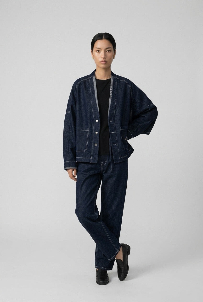 Denim jacket worn open over a black top, model with one hand on hip