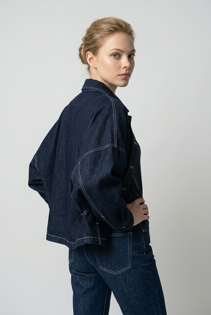 Model looking over her shoulder, showing white topstitching on the back of the denim jacket