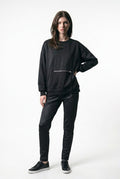 Model wearing the TOFUITO Zip Pocket Sweatshirt in black with a silver zip pocket at the front, black trousers and black sneakers, on a white background