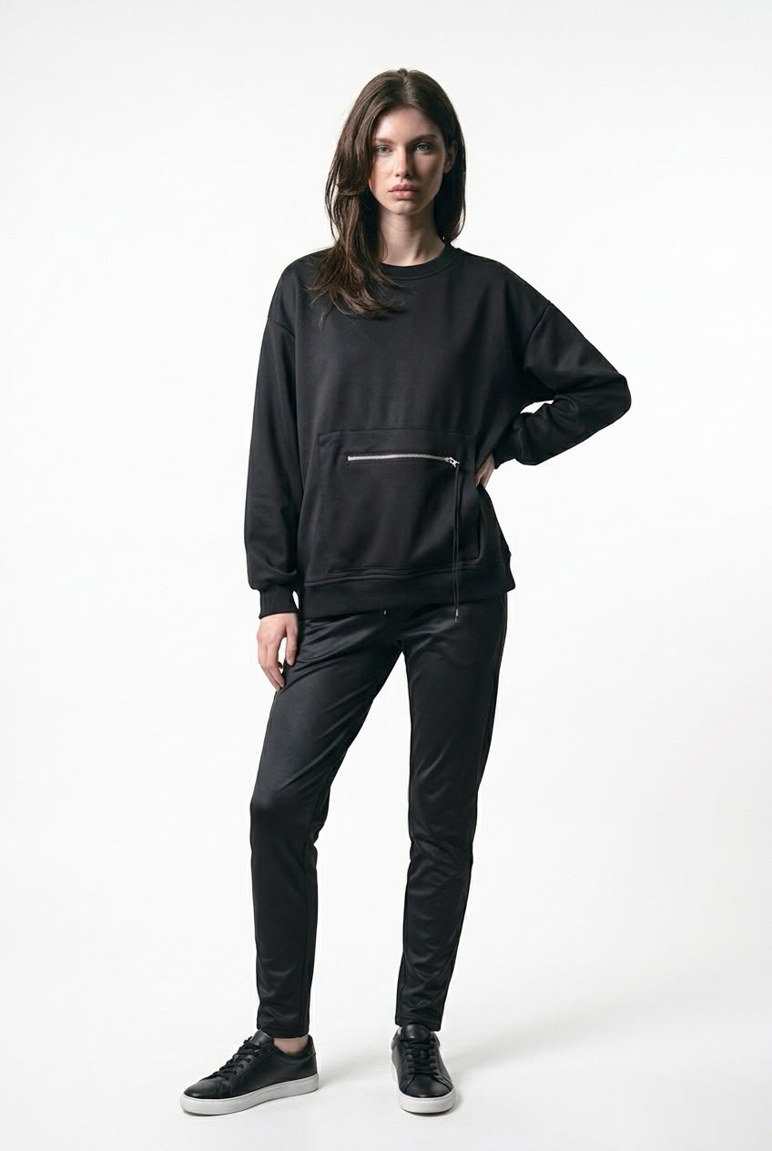 Model wearing the TOFUITO Zip Pocket Sweatshirt in black with a silver zip pocket at the front, black trousers and black sneakers, on a white background