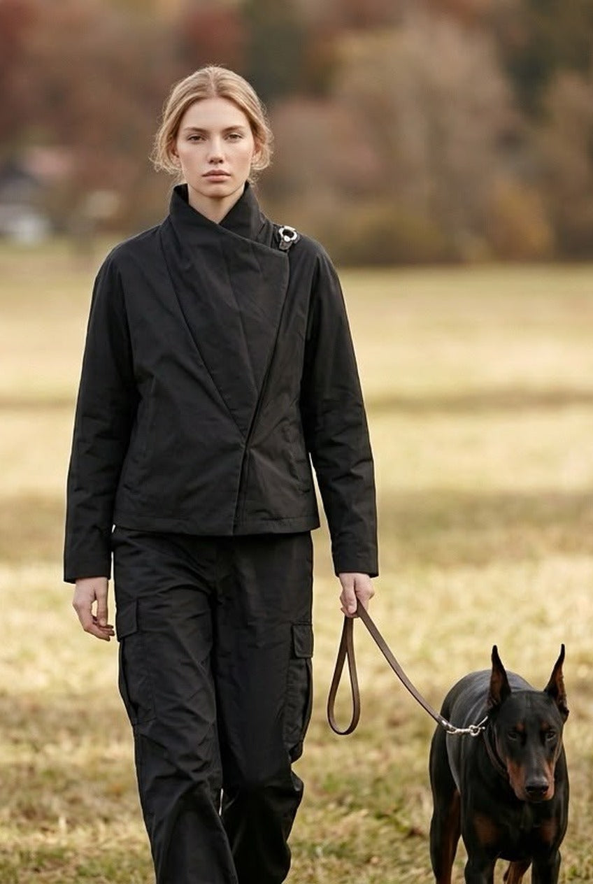 ブラック 中綿ジャケット－秋の野原で犬を連れて歩くモデル。肩のリングで重ね襟を留め、黒のカーゴパンツに合わせて