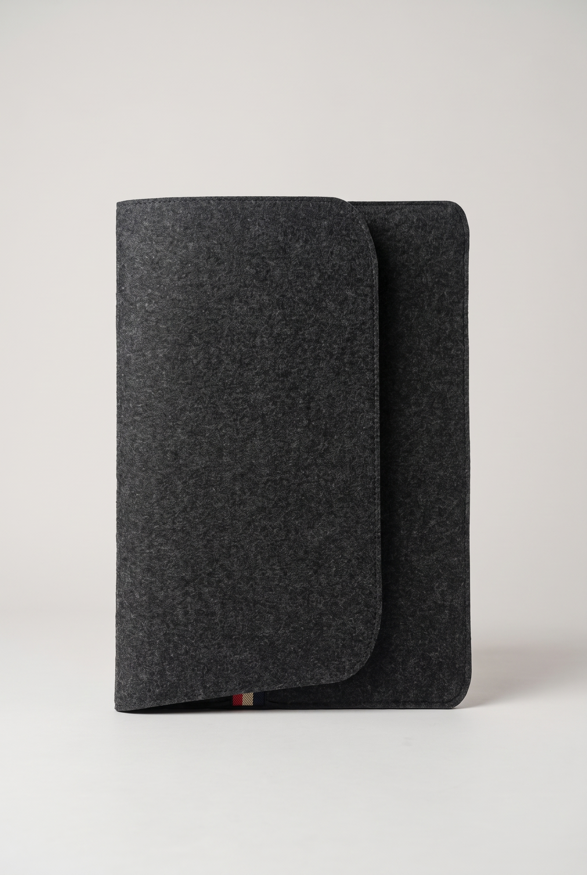 Angled view of the closed charcoal felt laptop sleeve with cover flap and striped tab