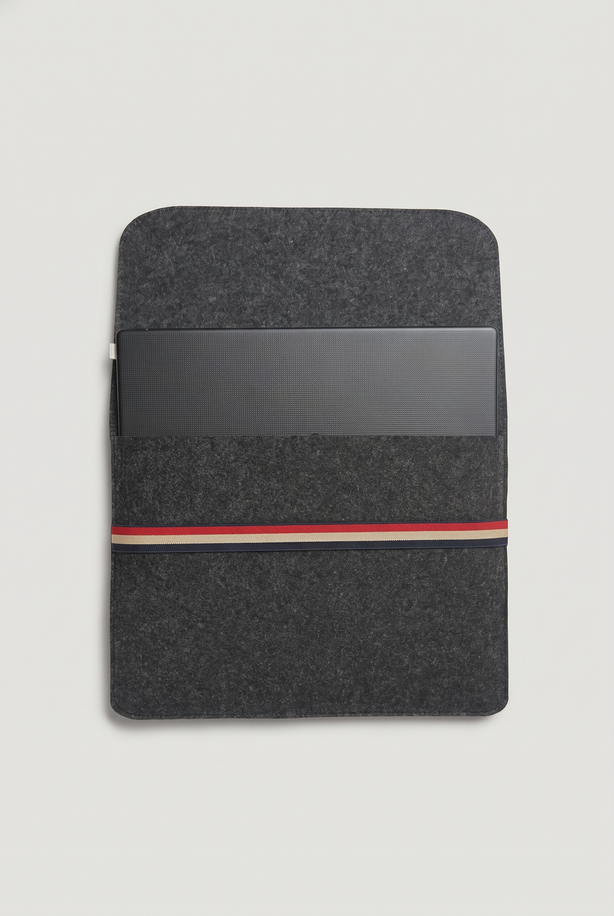Laptop placed inside the open charcoal felt sleeve, ready to fold the cover and secure with the striped elastic band (laptop not included)